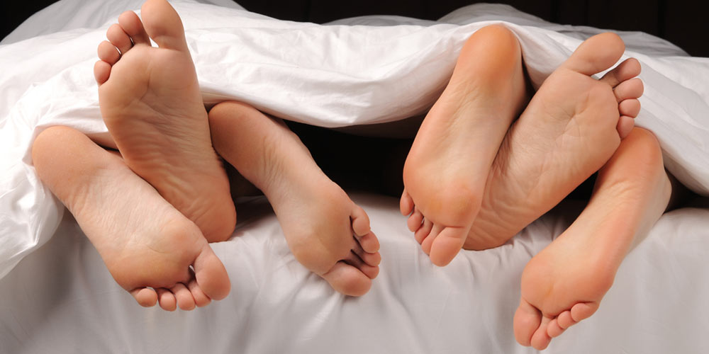 Three pairs of feet peeking out from under the covers on a bed